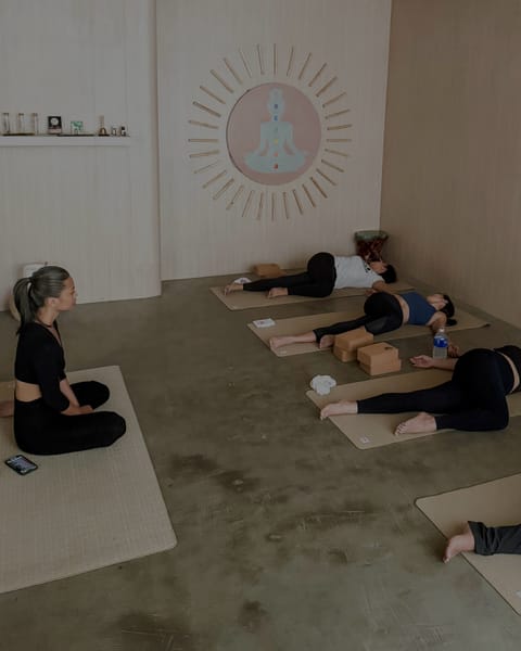 Joahnna seated on a mat guiding a group through a supported Yin pose